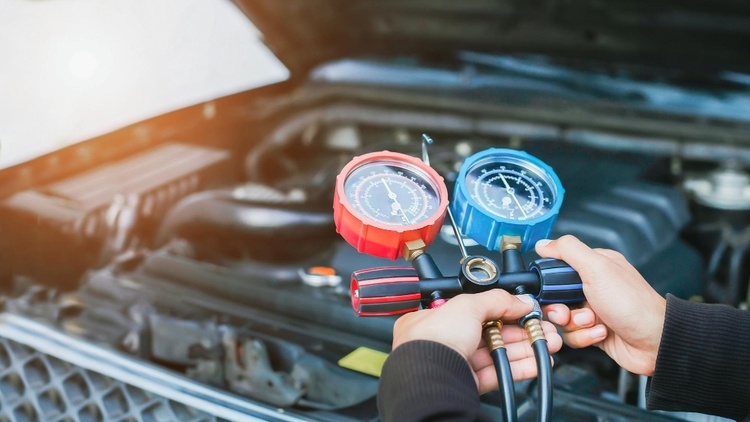 A person using a manifold gauge set with red and blue dials to check refrigerant levels in a car engine during routine car services in Singapore.